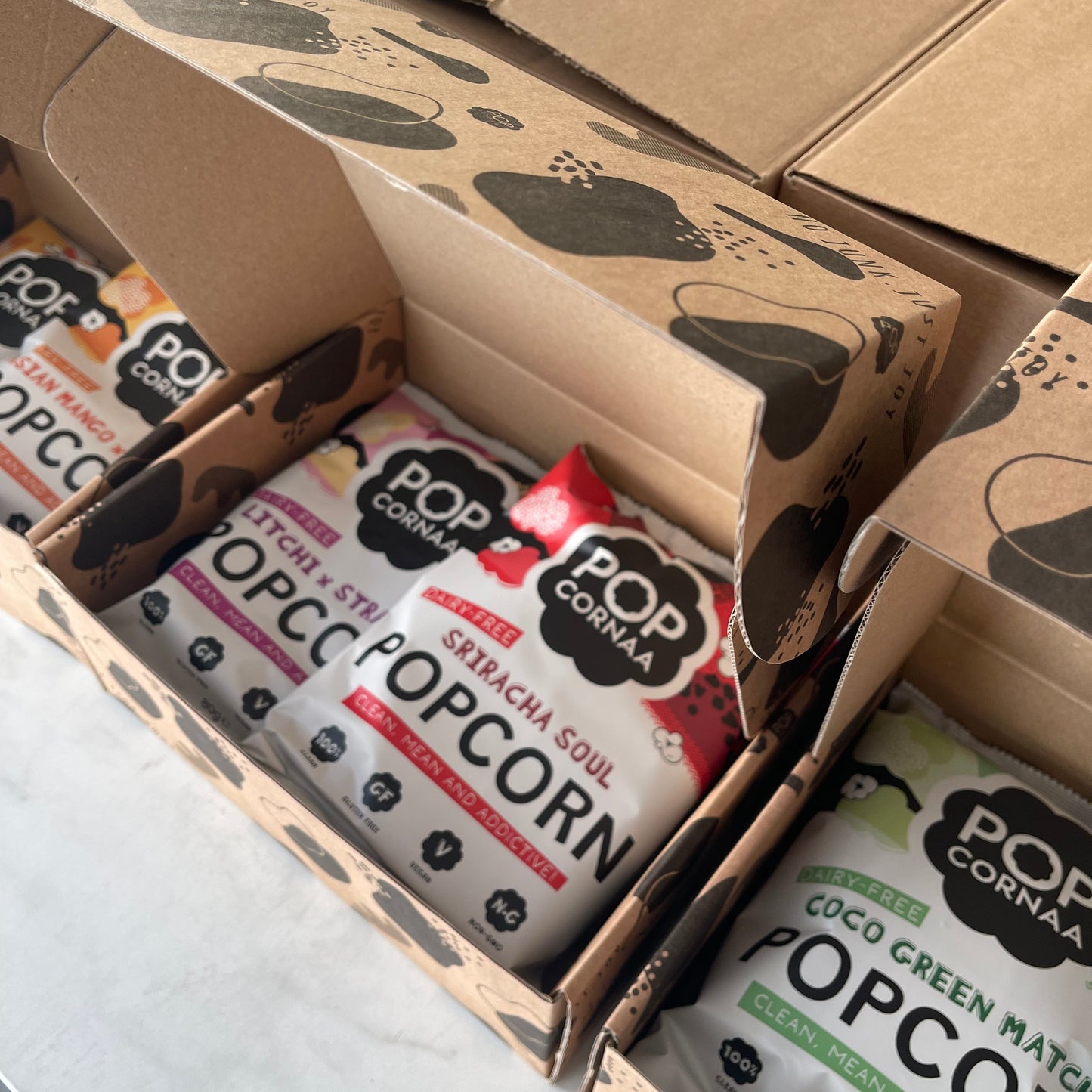 Popcorn packets in a PopCornaa Asian Fusion Taster cardboard box on a light background