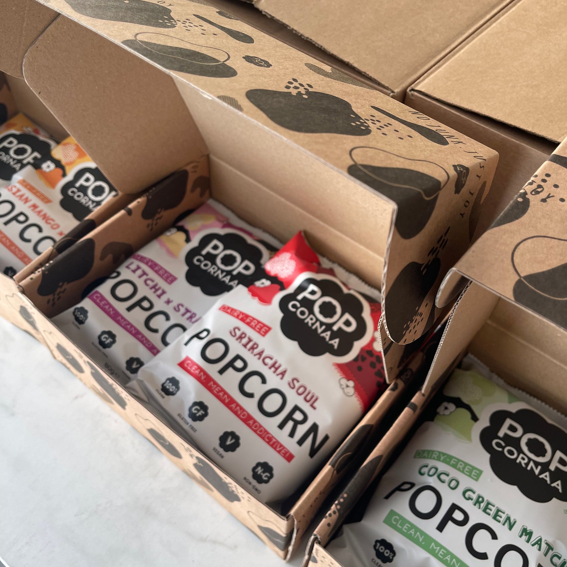Popcorn packets in a PopCornaa Asian Fusion Taster cardboard box on a light background