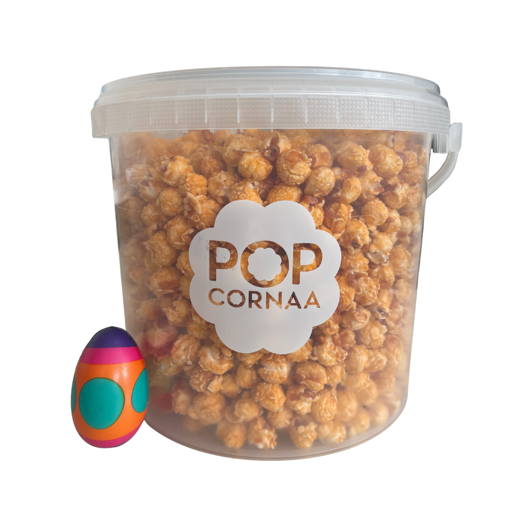 Bucket of 100% clean, diary free caramel  popcorn with 'POPCORNAA' label next to a colorful egg on a white background